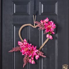 a heart shaped wreath with pink flowers hanging on the front door