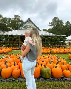 a woman holding a baby standing in front of pumpkins