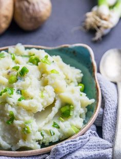 mashed potatoes with green onions in a bowl on a blue tablecloth next to silverware