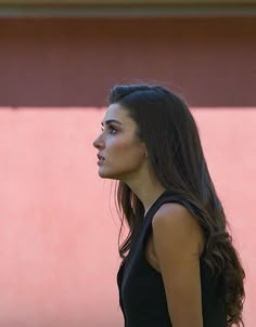 a woman standing in front of a pink wall with her hand on her hip and looking off to the side