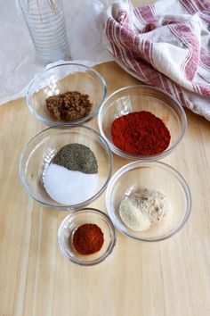 four bowls filled with different types of spices on top of a wooden table next to a glass bottle