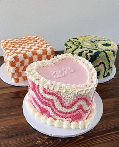 three cakes with different designs on them sitting on top of a wooden table next to each other