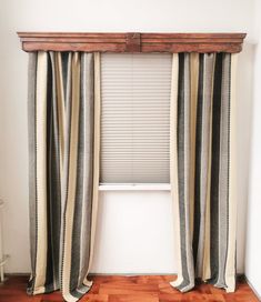 an empty room with wooden floors and striped curtains on the window sill, next to a radiator