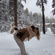 a man and woman kissing in the snow with trees behind them on a cloudy day