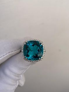 a blue cushion cut ring with diamonds on it's sides, in front of a plain white background