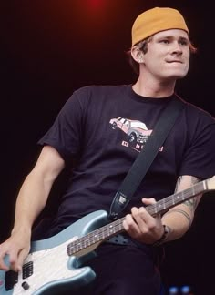 a young man playing an electric guitar while wearing a yellow hat and black t - shirt