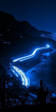 an aerial view of the ocean at night with lights in the water and mountains behind it