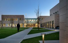 a person walking down a walkway in front of a building with lights on the grass