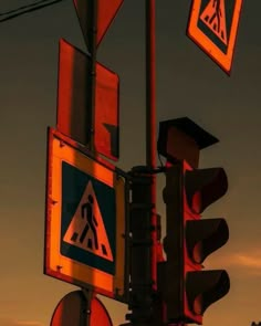 traffic lights and street signs are lit up at night time with the sun setting in the background