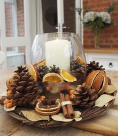 a candle is lit in a glass bowl filled with pine cones, oranges and cinnamons