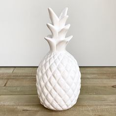 a white ceramic pineapple shaped vase sitting on a wooden floor