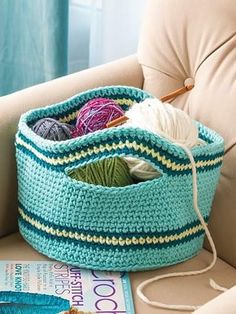 a blue crocheted basket with yarn in it on a chair next to a book