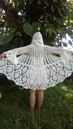 a woman wearing a white crocheted shawl standing in the grass with her back to the camera