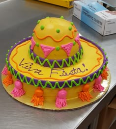 a yellow cake with pink, green and purple decorations sits on a silver countertop