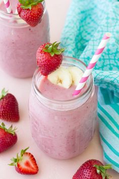 two mason jars filled with smoothie and strawberries next to one another on a blue towel