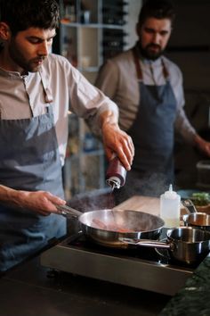 two men in aprons are cooking on the stove