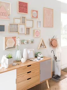 a wall with many pictures on it and some plants in vases next to the dresser