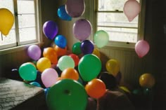 a bunch of balloons floating in the air near a laptop on a table with two windows