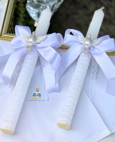 two white candles with bows on them sitting in front of a mirror