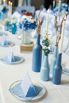 the table is set with blue vases and napkins, candles, and plates