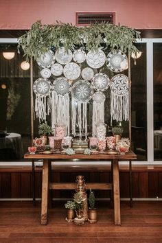 a wooden table topped with plates covered in tassels next to a window filled with potted plants