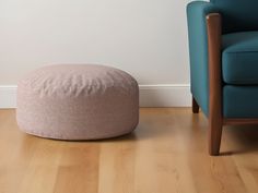 a living room with a blue chair and a pink round pouff on the floor