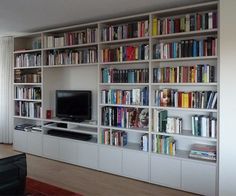 a living room filled with lots of books and a flat screen tv sitting on top of a book shelf