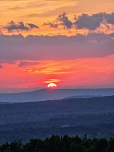 the sun is setting over some hills and trees