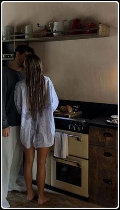 two people are standing in the kitchen looking at something on the stove top and oven