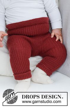 a baby sitting on top of a white pillow wearing red pants and holding his hands out