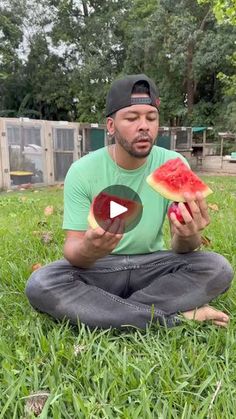 a man is sitting in the grass and holding a piece of watermelon with one hand