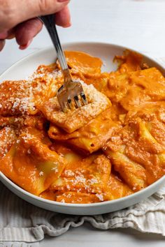 a person holding a fork in a bowl of food with sauce and cheese on top