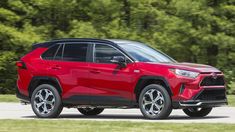 a red toyota rav driving down a road next to green grass and trees in the background