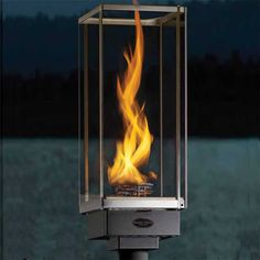 a fire burning inside of a glass box on top of a metal pole with water in the background