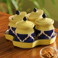 four yellow and blue ceramic teapots on a wooden table next to a small bowl