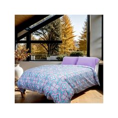 a bed with purple and blue comforter in front of a large window overlooking trees