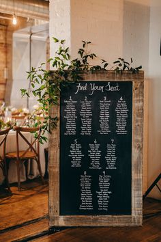 the seating plan is displayed on an old wooden board in front of a table with white linens and greenery