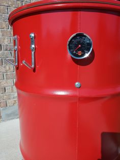 a large red barrel sitting on top of a sidewalk next to a brick wall with a thermometer in it