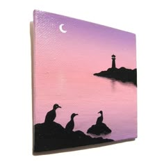 two ducks are sitting on the rocks by the water at sunset with a lighthouse in the distance