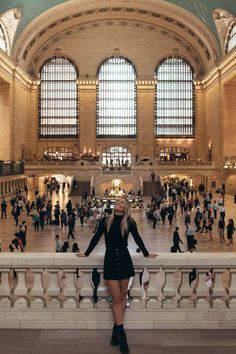 a woman standing in the middle of a train station with lots of people around her