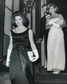 an old black and white photo of two women in evening dresses walking down the stairs