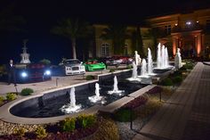 two cars parked in front of a fountain at night