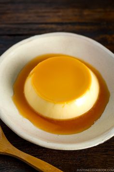 a white bowl filled with caramel sauce on top of a wooden table next to a spoon