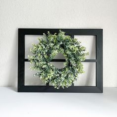 a black frame with a green wreath on it and a white wall in the background