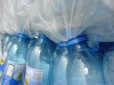 several blue bottles are lined up on the shelf together, with plastic bags around them