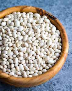 a wooden bowl filled with white beans on top of a blue counter next to a knife