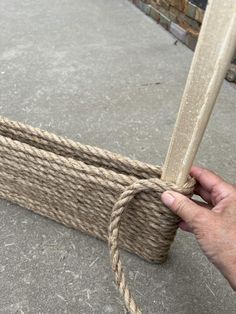 a hand holding a rope that has been tied to a wooden frame on the ground