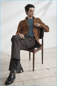 a man sitting on top of a wooden chair wearing a brown coat and black shoes