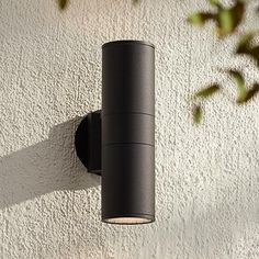 an outdoor light mounted on the side of a white stucco wall next to a plant