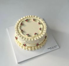 there is a white cake with red flowers on it sitting on top of a card